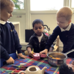 Three male pupils are playing chef, with a saucepan and teapot on the table in front of them 